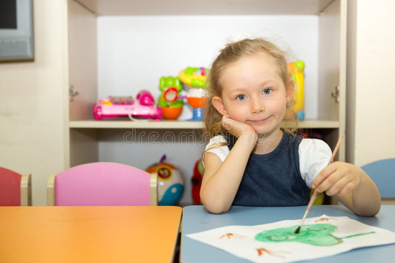 Adorable child girl draws a brush and paints in nursery room. Kid in kindergarten in Montessori preschool class. Adorable child girl draws a brush and paints in stock image
