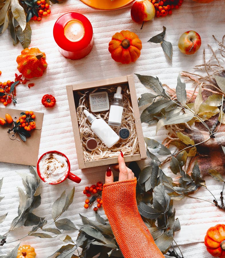 Beauty and autumn skin care concept. Female hand in orange knitted sweater opens beauty box with cosmetic products on desktop with royalty free stock photo