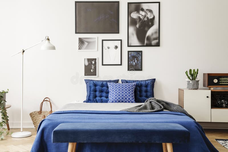 Bench in front of bed with navy blue pillows between lamp and cabinet in bedroom interior. Real photo. Concept royalty free stock photos