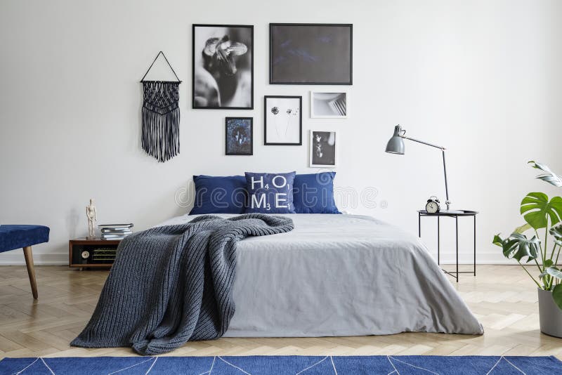 Blanket on bed with blue pillows in white bedroom interior with gallery and lamp on table. Real photo. Concept stock photo