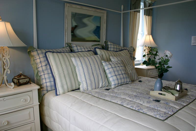 Blue Bedroom. Blue and white bedroom showing bed with variety of square pillows and bedspread, blue walls, white dresser and iron lamps stock image