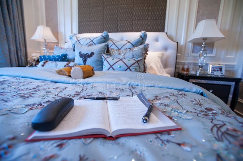 A book in a Blue Bedroom in a mansion. Blue Bedroom in a mansion,blue silk Quilt.Soft pillow.White lamps.Wood decoration.A book laid on the bed stock image