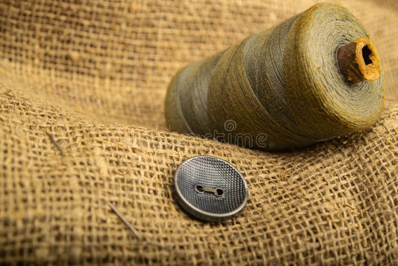 Button sewn to burlap with a rough texture and a spool of thread. Close up.  stock photos