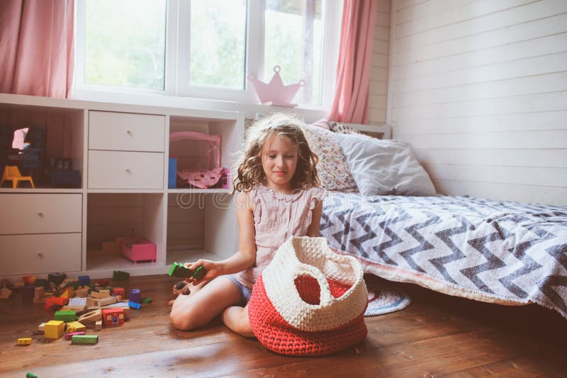 Child girl cleaning her room and organize wooden toys into knitted storage bag. Housework and help concept stock photo