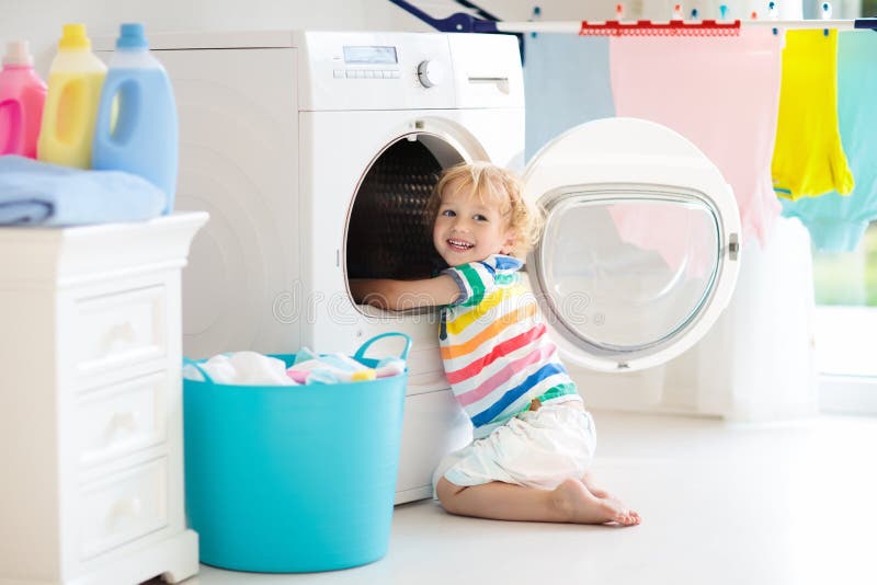 Child in laundry room with washing machine. Or tumble dryer. Kid helping with family chores. Modern household devices and washing detergent in white sunny home stock photo