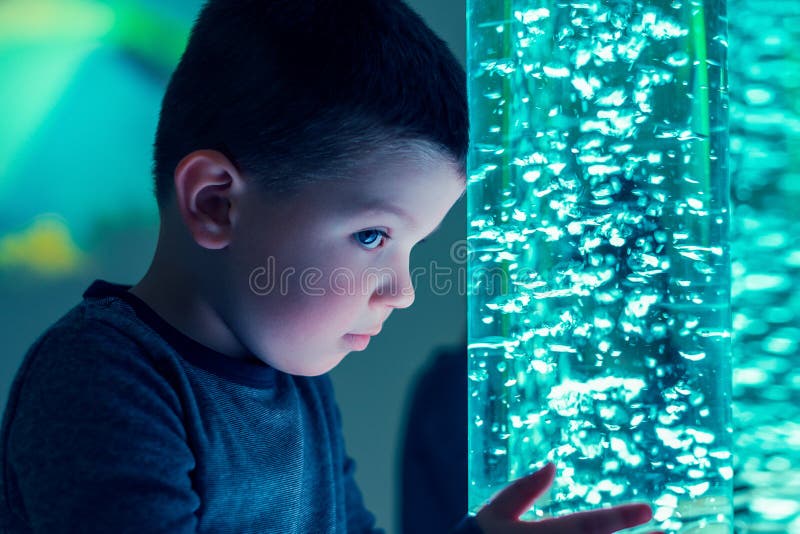 Child in therapy sensory stimulating room, snoezelen. Child interacting with colored lights bubble tube lamp during therapy. Child in therapy sensory stock photo
