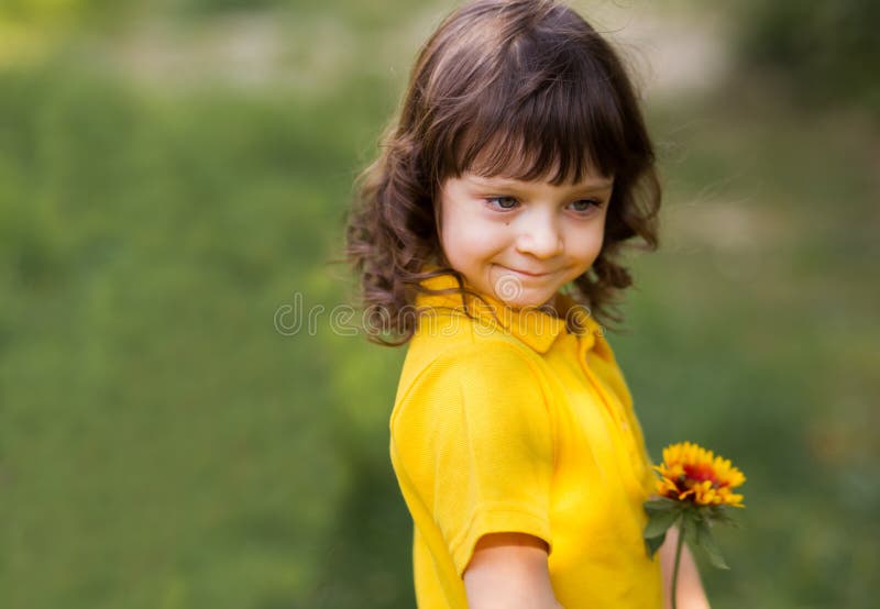 Close-up portrait of a cute curly girl kid in a yellow T-shirt and in nature stock image