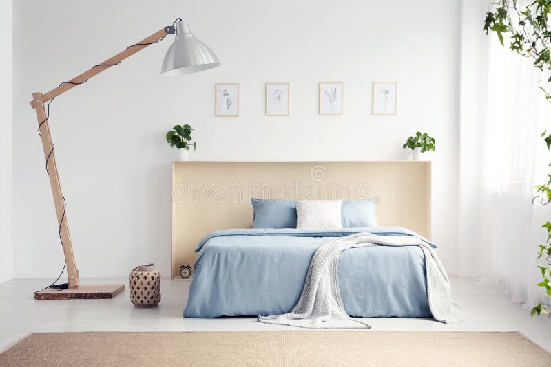 Designer lamp next to blue bed with blanket in white bedroom int. Erior with posters. Real photo royalty free stock image