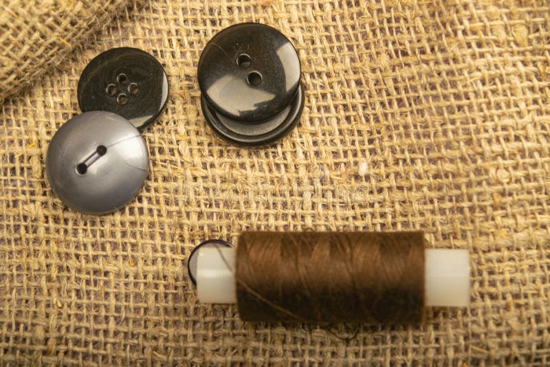 Different buttons and a spool of thread on the burlap with a rough texture. Close up.  stock photos
