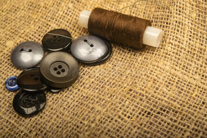 Different buttons and a spool of thread on the burlap with a rough texture. Close up.  stock images