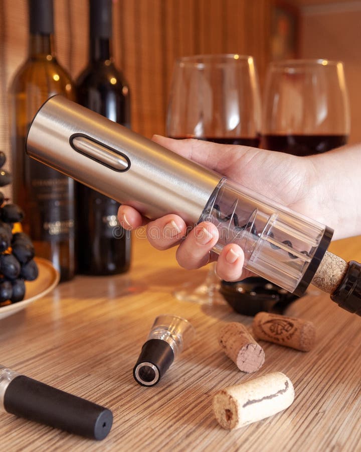 Female hand holds an electric corkscrew. And he opens a bottle of wine. In the background are bottles of wine, glasses and grapes stock photography