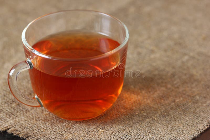 Glass transparent mug with black tea on rough burlap tablecloth.  stock photography