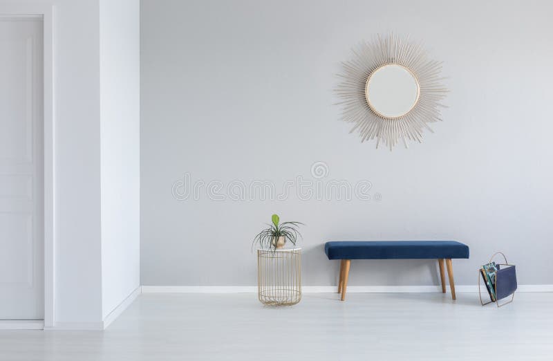 Gold mirror on the wall above blue bench in minimal empty entrance hall interior with plant. Real photo stock photography