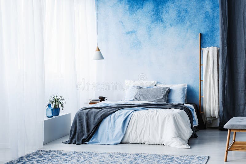 Grey and blue bedding on bed against ombre wall in minimal bedroom interior with ladder royalty free stock photos