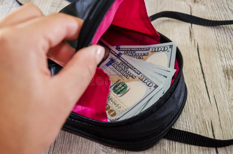 Hand opens a backpack with dollars on a wooden background stock image