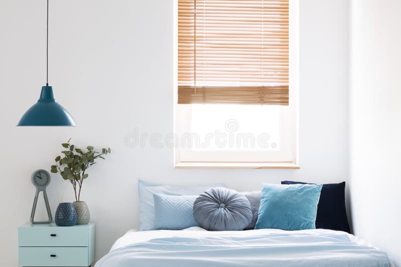 Lamp above blue cabinet with plant next to bed in simple bedroom. Interior with window. Real photo royalty free stock image