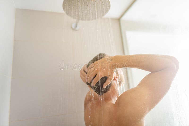 Man taking a shower washing hair under water falling from rain showerhead in luxury walk-in bath. Showering young person. At home lifestyle. Body care morning royalty free stock image