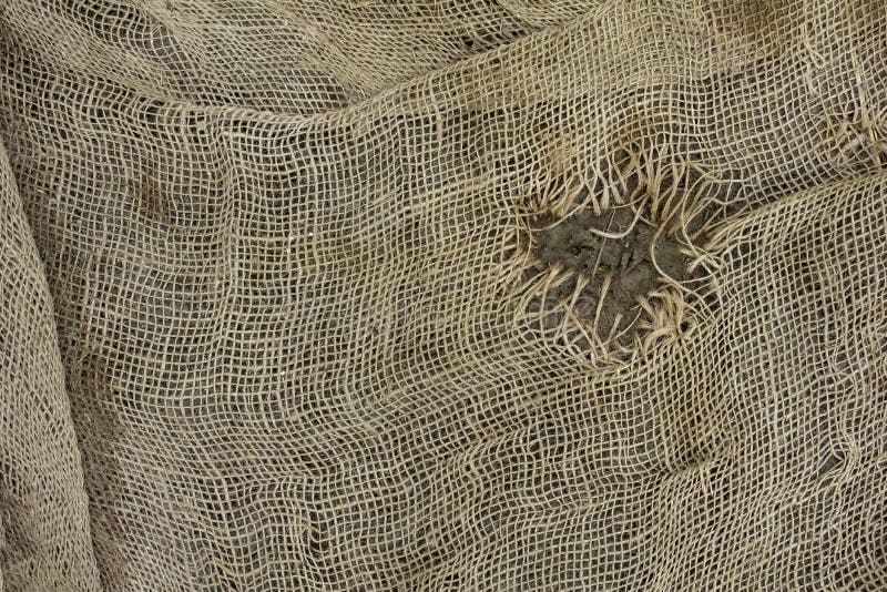 Old battered gray burlap mesh with a large burnt hole. rough surface texture. A old battered gray burlap mesh with a large burnt hole. rough surface texture royalty free stock image