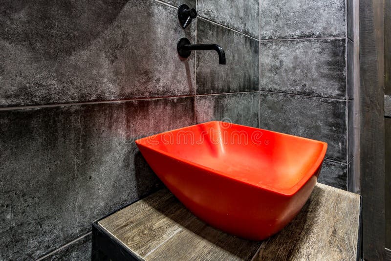 Red washbasin with faucet in expensive loft bathroom in elite sport bar on black brick wall background royalty free stock images