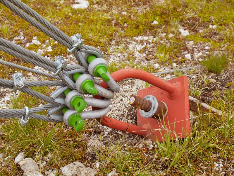 Sling and scrap in green yard, iron twisted rope fixed by screws snap hooks and grommets at anchor in ground. Sling and scrap in green yard, iron twisted rope royalty free stock image