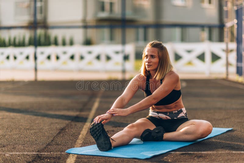 Sports. Woman on the sports ground doing stretching exercises and smiling on the floor royalty free stock images