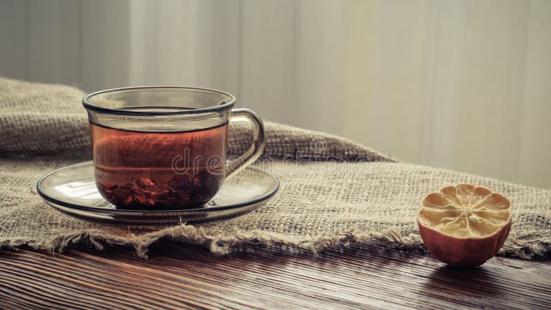 Tea in a transparent glass cup and dried lemon on the edge of a rough burlap tablecloth on old boards in natural light stock image