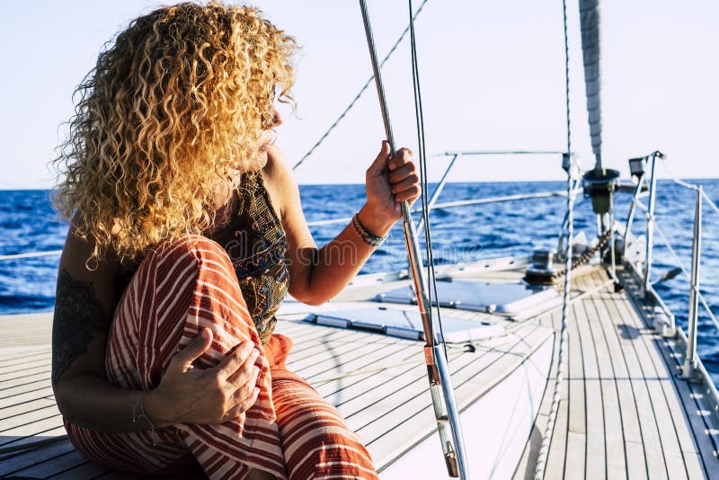 Travel and luxury lifestyle concept wtith beautiful blonde curly attractive woman sitting on the dock of a sail boat - people royalty free stock photo