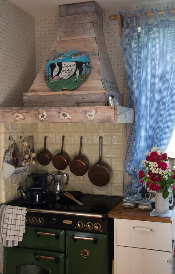 Vintage english kitchen from Poland. Kitchen with wooden hood, english stove, hand made piece of art, french saucepans hanging on the tiled wall. Fresh flowers stock photo