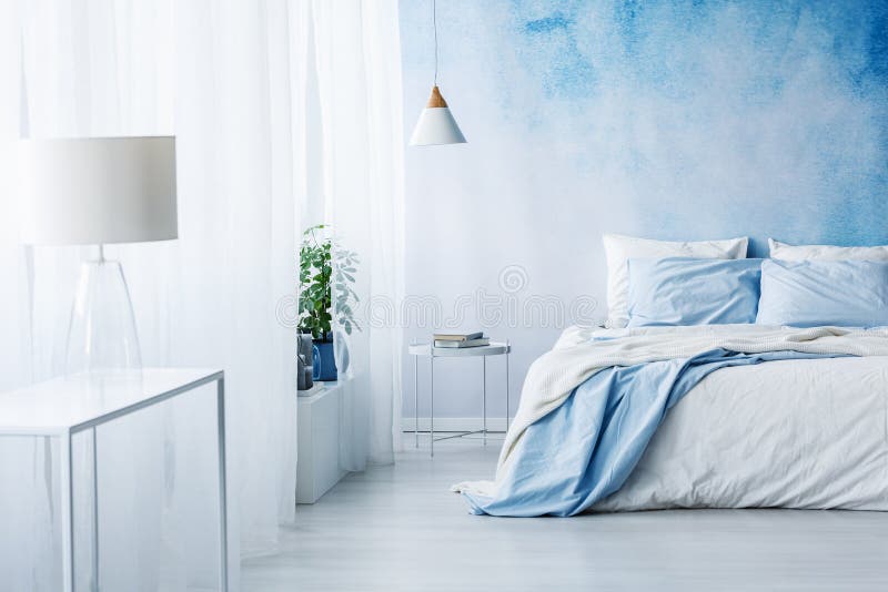 White lamp on a table in bright blue bedroom interior with bed a. Gainst ombre wall royalty free stock image