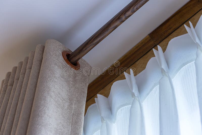 Window beige curtains and white tulle on the curtain rod. Close up stock photography