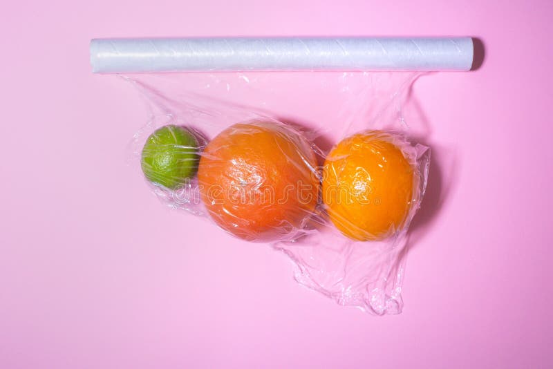 Wrapping plastic transparent food film on pink background packaging of citrus fruits, grapefruit, orange, lime. place for text, royalty free stock photos